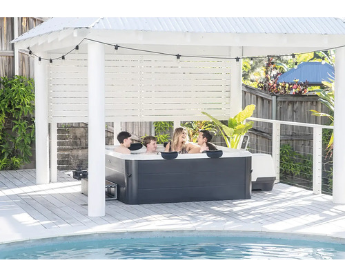 Rodina ve vířivce pod světlým pavilonem na dřevěné terase u bazénu se světelným řetězem.