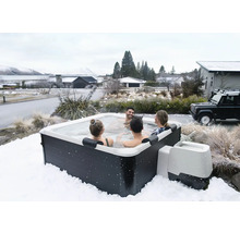 Čtvercová venkovní vířivka se čtyřmi osobami v zasněžené zimní krajině, tmavé obložení a bílá vnitřní vana.