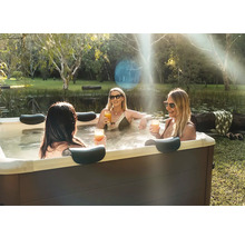 Tři ženy relaxují ve vířivce v zahradě u rybníka. Vířivka má tmavé obložení a opěrky hlavy.