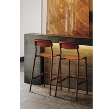 Dvě moderní barové stoličky v terakotové barvě u betonového pultu, dekorativní panel se vzhledem dřeva, atmosférické osvětlení.