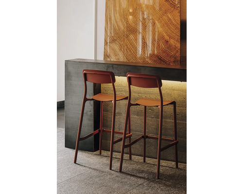 Dvě moderní barové stoličky v terakotové barvě u betonového pultu, dekorativní panel se vzhledem dřeva, atmosférické osvětlení.