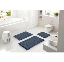 Světlá moderní koupelna se třemi modrými strukturovanými koupelnovými předložkami na bílé dlažbě, včetně vany, toalety a umyvadla.