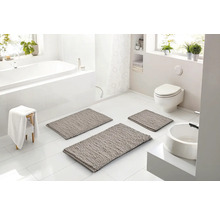 Světlá, moderní koupelna se třemi šedými koupelnovými předložkami na bílé dlažbě, vanou, toaletou a umyvadlem v bílé barvě.