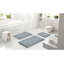 Světlá koupelna se třemi modrošedými koupelnovými předložkami různých velikostí, bílou vanou, toaletou a umyvadlem.