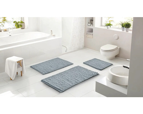 Světlá koupelna se třemi modrošedými koupelnovými předložkami různých velikostí, bílou vanou, toaletou a umyvadlem.