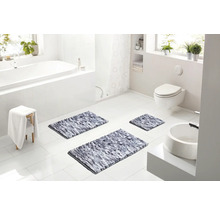 Světlá moderní koupelna s bílou vanou, toaletou a třemi šedými melírovanými koupelnovými předložkami na bílé dlažbě.