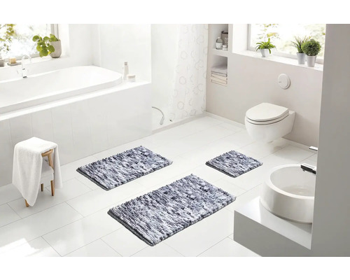 Světlá moderní koupelna s bílou vanou, toaletou a třemi šedými melírovanými koupelnovými předložkami na bílé dlažbě.