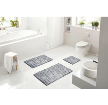 Světlá moderní koupelna s bílou vanou, závěsnou toaletou, umyvadlem a třemi šedými koupelnovými předložkami na podlaze.