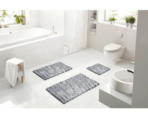 Světlá moderní koupelna s bílou vanou, závěsnou toaletou, umyvadlem a třemi šedými koupelnovými předložkami na podlaze.