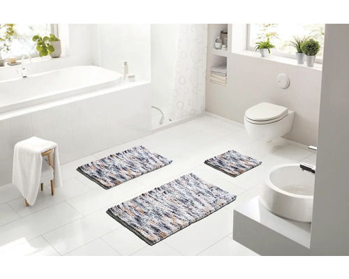 Světlá koupelna s vanou, toaletou a umyvadlem, vybavená třemi vícebarevnými koupelnovými předložkami různých velikostí.