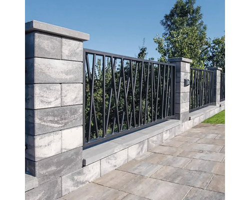 Moderní zahradní zeď z šedých tvárnic s tmavými kovovými prvky v geometrickém designu před stromy a kamennou podlahou.