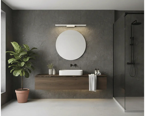 Moderní koupelna s kulatým zrcadlem, lineárním LED nástěnným svítidlem, závěsnou dřevěnou skříňkou pod umyvadlo, bílým umyvadlem na desku a sprchou.