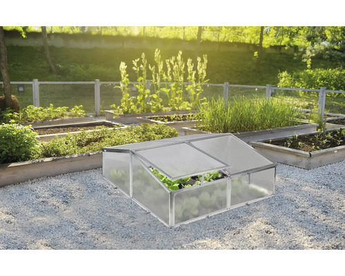 Malé pařeniště z hliníku a plastových desek v organizované zahradě s vyvýšenými záhony na štěrku.