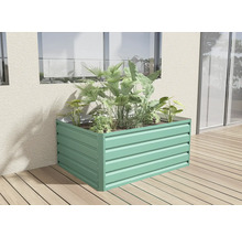 Obdélníkový kovový vyvýšený záhon ve světle zelené barvě, osázený zelenými rostlinami na dřevěné terase u stěny domu.