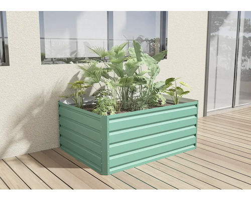 Obdélníkový kovový vyvýšený záhon ve světle zelené barvě, osázený zelenými rostlinami na dřevěné terase u stěny domu.
