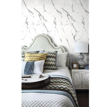 Světlá ložnice s tapetou ve vzhledu mramoru, postel s polstrovaným čelem, vzorované polštáře a noční stolek s lampičkou.