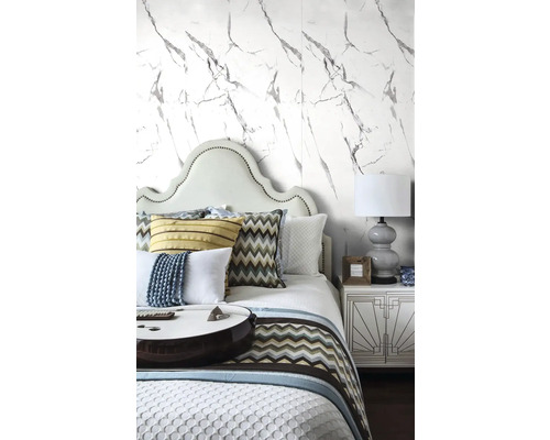 Světlá ložnice s tapetou ve vzhledu mramoru, postel s polstrovaným čelem, vzorované polštáře a noční stolek s lampičkou.