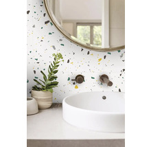 Moderní koupelna s nástěnnými obklady s terazzo vzorem, bílým umyvadlem na desku a bronzovou nástěnnou baterií.