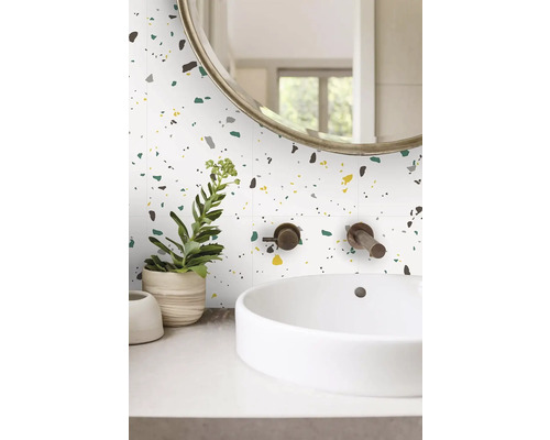 Moderní koupelna s nástěnnými obklady s terazzo vzorem, bílým umyvadlem na desku a bronzovou nástěnnou baterií.