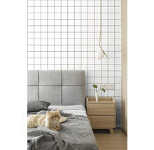 Tapeta s mřížkovým vzorem v ložnici s šedým polstrovaným čelem postele, dřevěným nočním stolkem a moderním závěsným svítidlem.