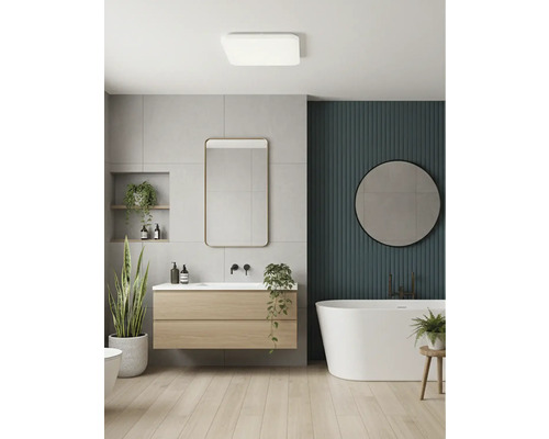 Moderní koupelna s dřevěnou skříňkou pod umyvadlo, volně stojící vanou, zrcadly, šedými obklady a zelenou lamelovou stěnou.