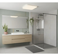 Moderní koupelna se závěsnou skříňkou v dekoru dřeva, bílým umyvadlem, zrcadlem a sprchovým koutem s černým rámem.