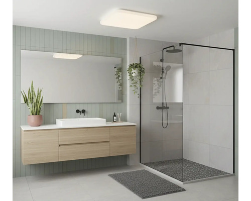 Moderní koupelna se závěsnou skříňkou v dekoru dřeva, bílým umyvadlem, zrcadlem a sprchovým koutem s černým rámem.