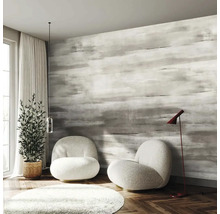 Moderní pokoj s šedou tapetou se vzorem tahů štětcem, dvěma bílými křesly, parketami v podobě rybí kosti a pokojovou rostlinou.