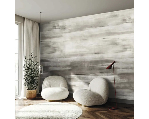 Moderní pokoj s šedou tapetou se vzorem tahů štětcem, dvěma bílými křesly, parketami v podobě rybí kosti a pokojovou rostlinou.