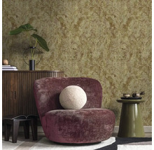 Strukturovaná tapeta s ornamentálním vzorem ve zlaté a zelené barvě v obývacím pokoji s fialovým křeslem a dřevěnou komodou.