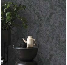 Tmavá vliesová tapeta s barokním vzorem a texturou, v kombinaci s pokojovou rostlinou a čajovou konvicí v moderně zařízeném pokoji.