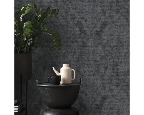 Tmavá vliesová tapeta s barokním vzorem a texturou, v kombinaci s pokojovou rostlinou a čajovou konvicí v moderně zařízeném pokoji.