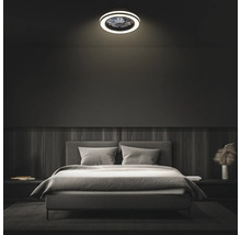Moderní stropní ventilátor s LED osvětlením v tmavě zařízené ložnici nad šedou čalouněnou postelí.