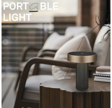 Moderní přenosná venkovní stolní lampa na dřevěném odkládacím stolku v uspořádaném balkónu s lehátky a polštáři.
