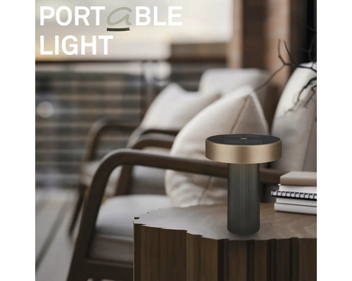 Moderní přenosná venkovní stolní lampa na dřevěném odkládacím stolku v uspořádaném balkónu s lehátky a polštáři.