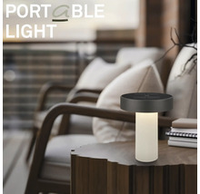 Přenosná stolní LED lampa na dřevěném stole v moderním venkovním prostoru s pohodlnými křesly.