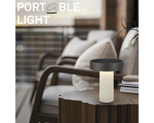 Přenosná stolní LED lampa na dřevěném stole v moderním venkovním prostoru s pohodlnými křesly.