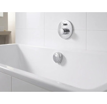 Podomítková vanová baterie a přepadová souprava z chromu u bílé vany ve světlé, organizované koupelně.