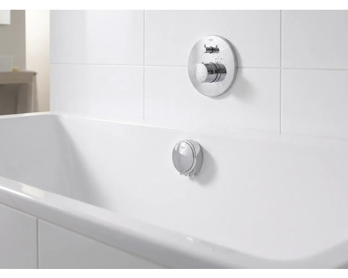 Podomítková vanová baterie a přepadová souprava z chromu u bílé vany ve světlé, organizované koupelně.