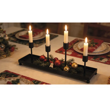 Adventní svícen z černého kovu se čtyřmi držáky na svíčky, zdobený jedlovým chvojím a vánočními ozdobami na slavnostně prostřeném stole.
