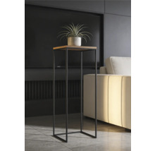 Moderní vysoký stojan na rostliny s čtvercovou dřevěnou deskou a černým kovovým rámem v osvětleném obývacím pokoji vedle pohovky.