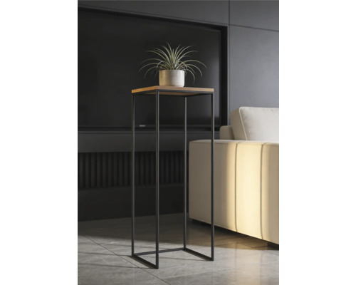 Moderní vysoký stojan na rostliny s čtvercovou dřevěnou deskou a černým kovovým rámem v osvětleném obývacím pokoji vedle pohovky.