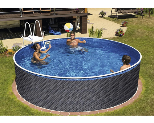 Kulatý nadzemní bazén s ratanovým vzhledem a modrou vnitřní fólií na zahradě, kde si tři lidé hrají s nafukovacím míčem.