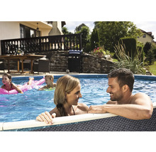 Rodina v zahradním bazénu s ratanovým vzhledem. V pozadí dům s terasou, plynový gril a zahrada.