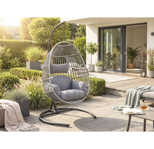 Moderní závěsné křeslo z šedého umělého ratanu s polštáři na světlé terase v prosluněné zahradě.