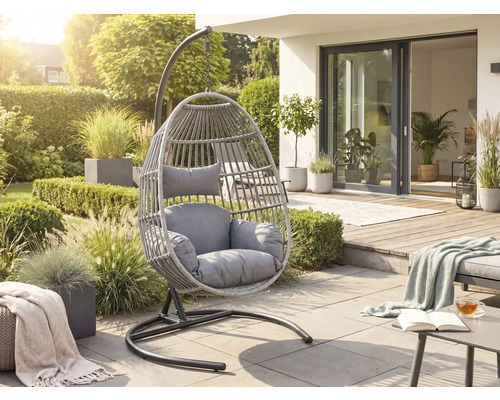Moderní závěsné křeslo z šedého umělého ratanu s polštáři na světlé terase v prosluněné zahradě.