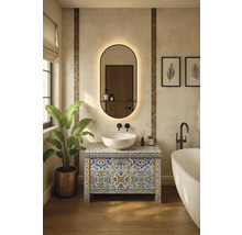 Moderní koupelna s dlaždicovou skříňkou pod umyvadlo, umyvadlem na desku, oválným zrcadlem s osvětlením, volně stojící vanou a rostlinou.