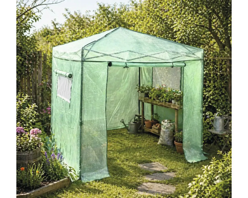 Průchozí fóliovník na zahradě s dřevěným regálem, rostlinami v květináčích, konví a pytlem se zeminou na trávníku.