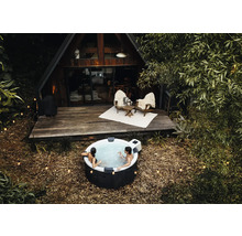 Lidé relaxují v kulaté nafukovací vířivce venku před dřevěným domem ve tvaru A s terasou a světelnými řetězy.