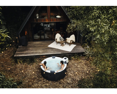 Lidé relaxují v kulaté nafukovací vířivce venku před dřevěným domem ve tvaru A s terasou a světelnými řetězy.